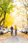 Two students ride down Greek Row in the fall, amid changing leaves.